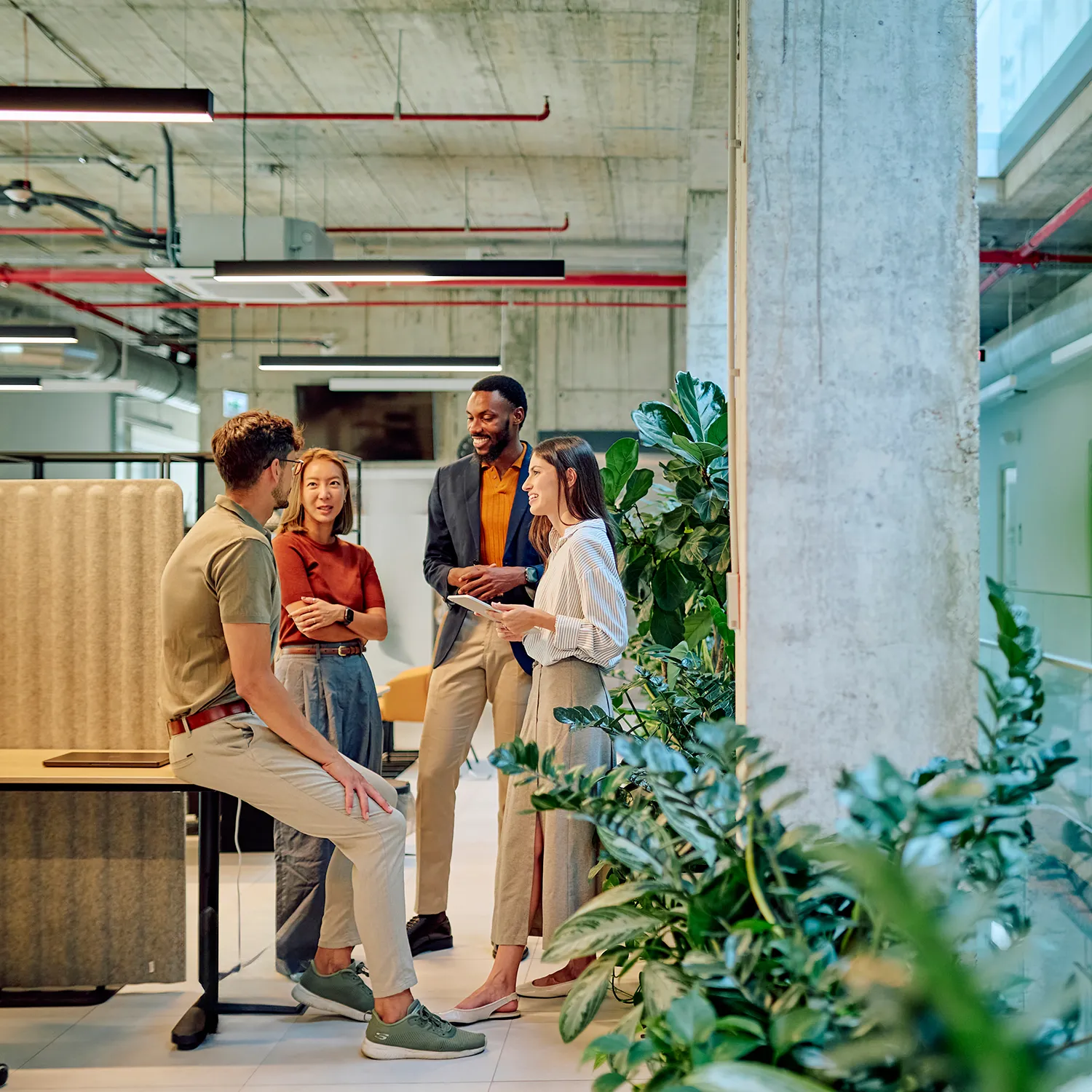 A group of employees networking and chatting near a vibrant green wall installation in an office lounge.