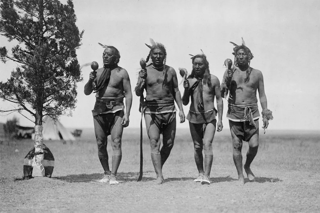 A historical black-and-white photograph of Native American men walking across the plains.