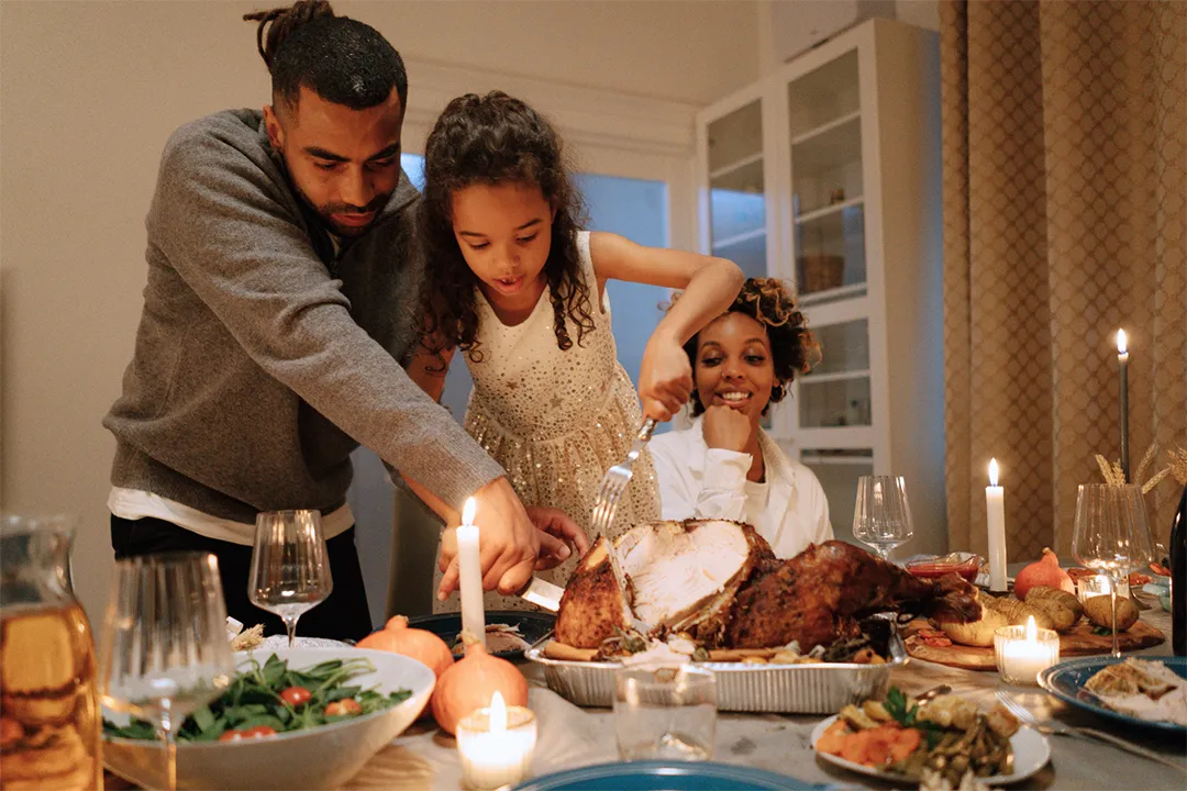 Family carving a turkey at a Thanksgiving dinner table, surrounded by seasonal dishes like mashed potatoes, cranberry sauce, and pumpkin pie.