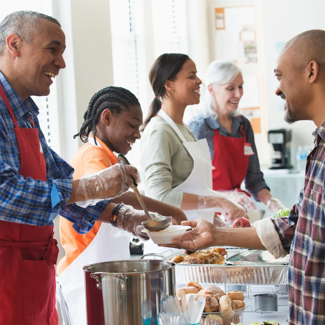 Volunteers smiling as they serve food to people.