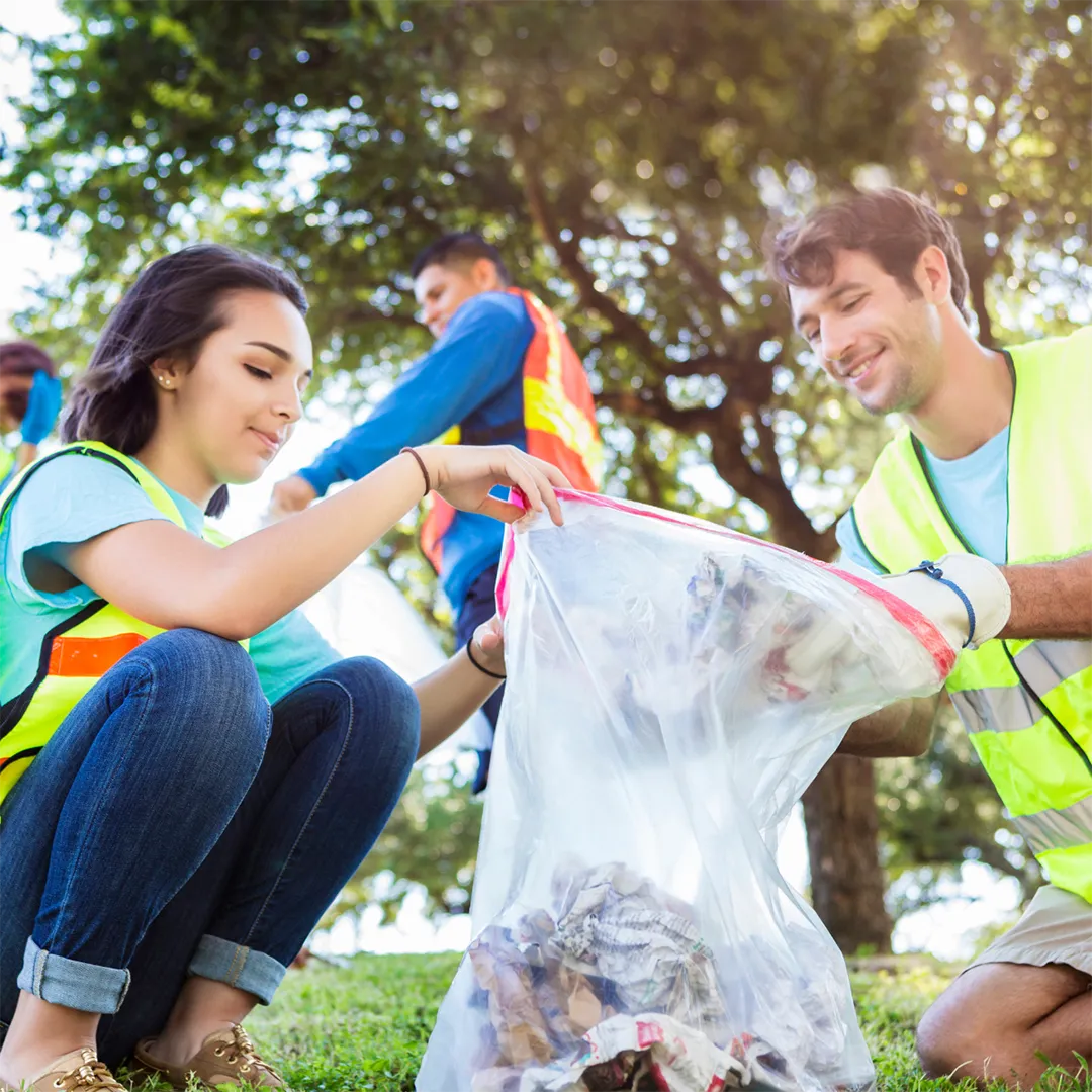 Volunteers cleaning a park, placing litter into a garbage bag.