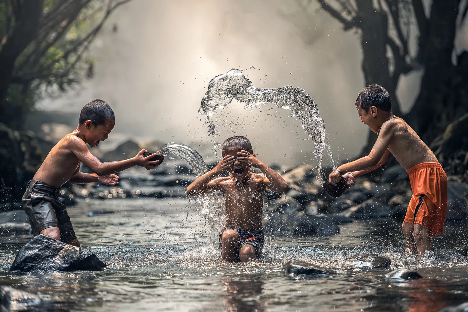 Three kids play in the river's water, happily splashing each other.