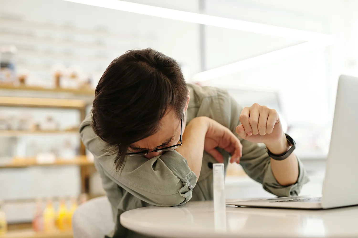 Office employee sneezing into arm inside of a plantless office environment.