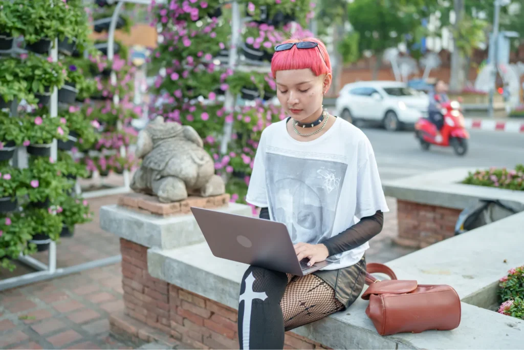 A young person working on a laptop beside a display of vibrant pink flowers.