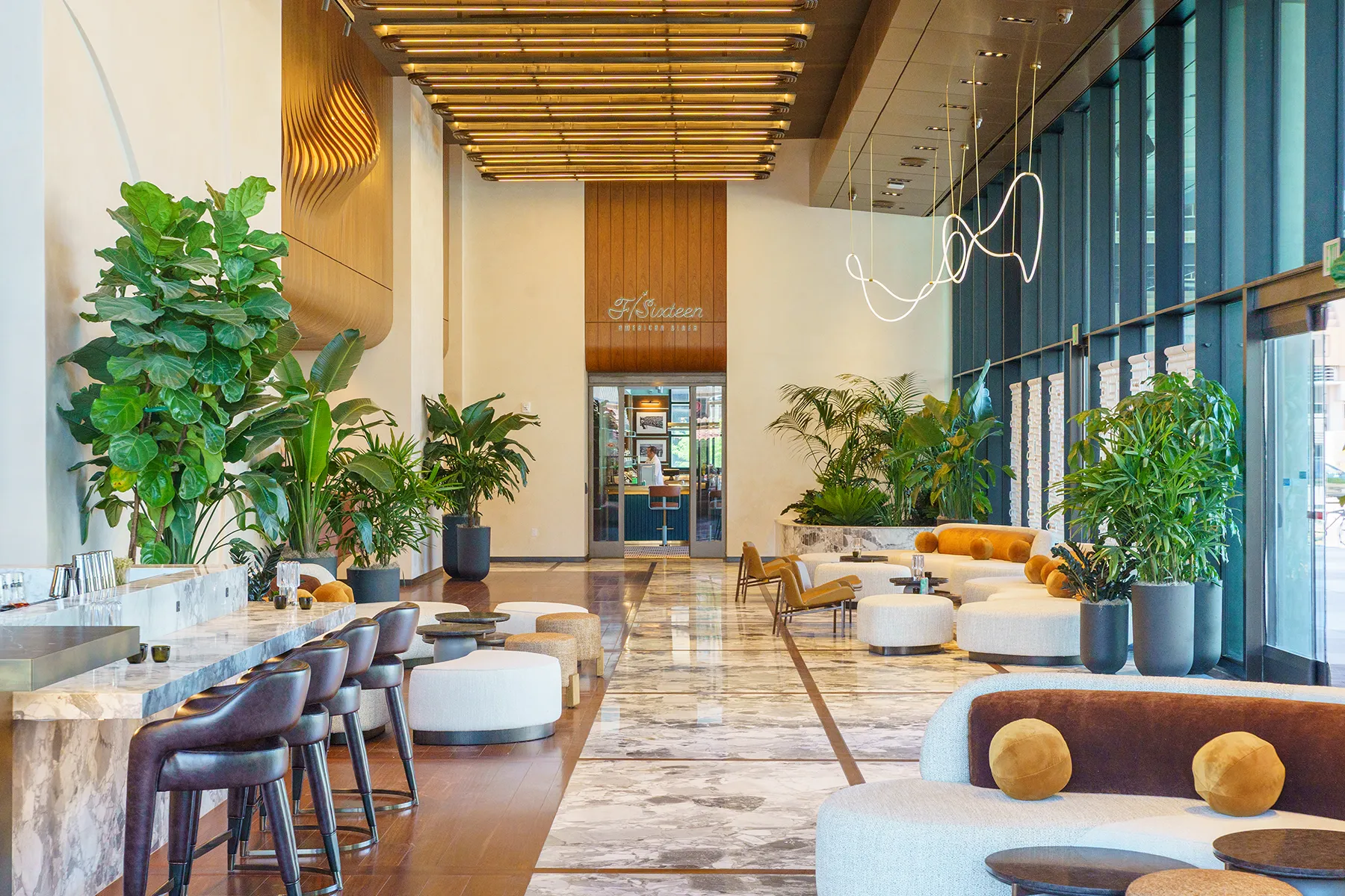 A spacious hotel lobby featuring extensive interior landscape design, including large potted indoor plants and natural lighting.
